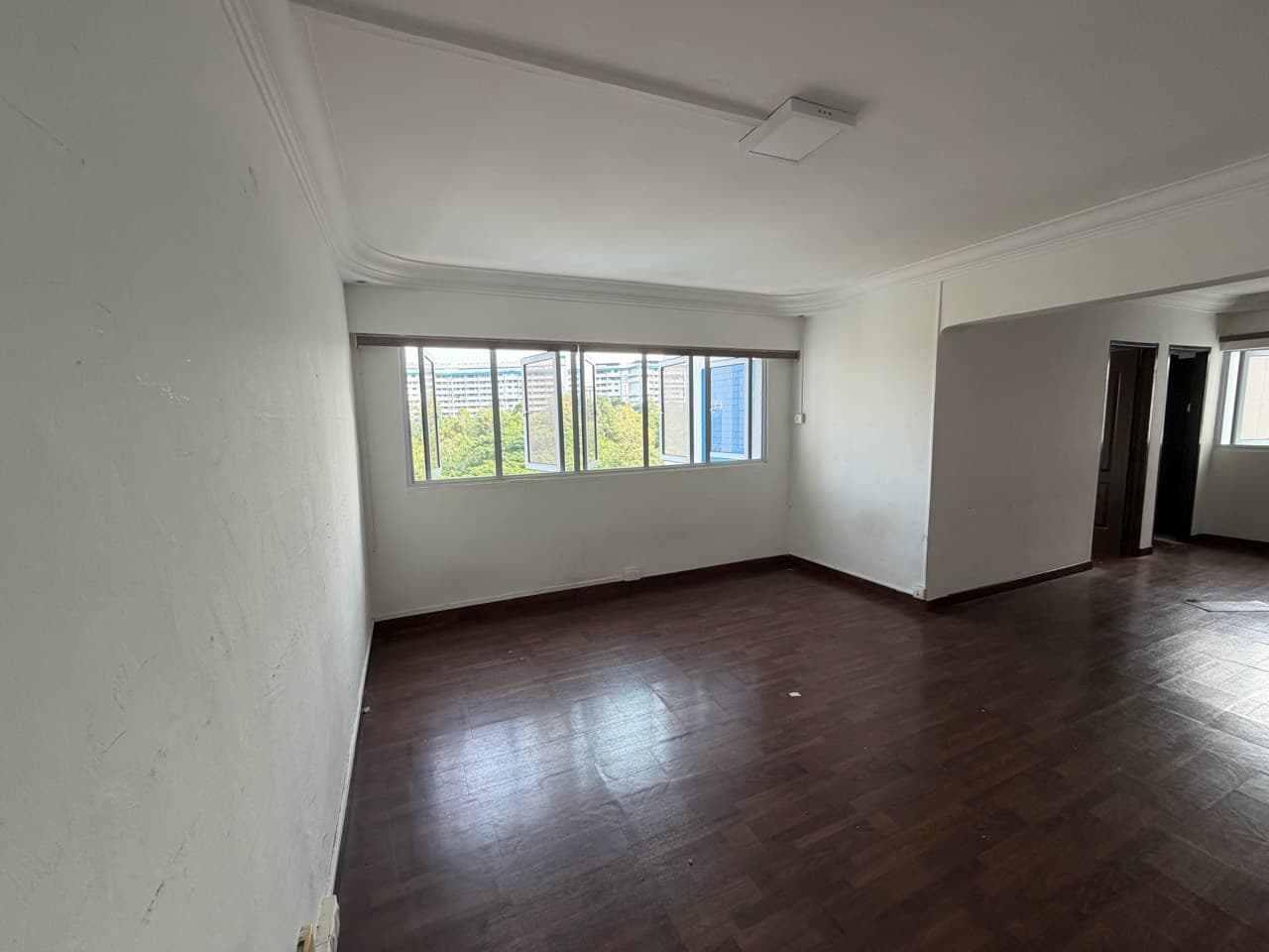 Actual site photograph of the HDB living room before renovation, with dark timber flooring and a window wall
